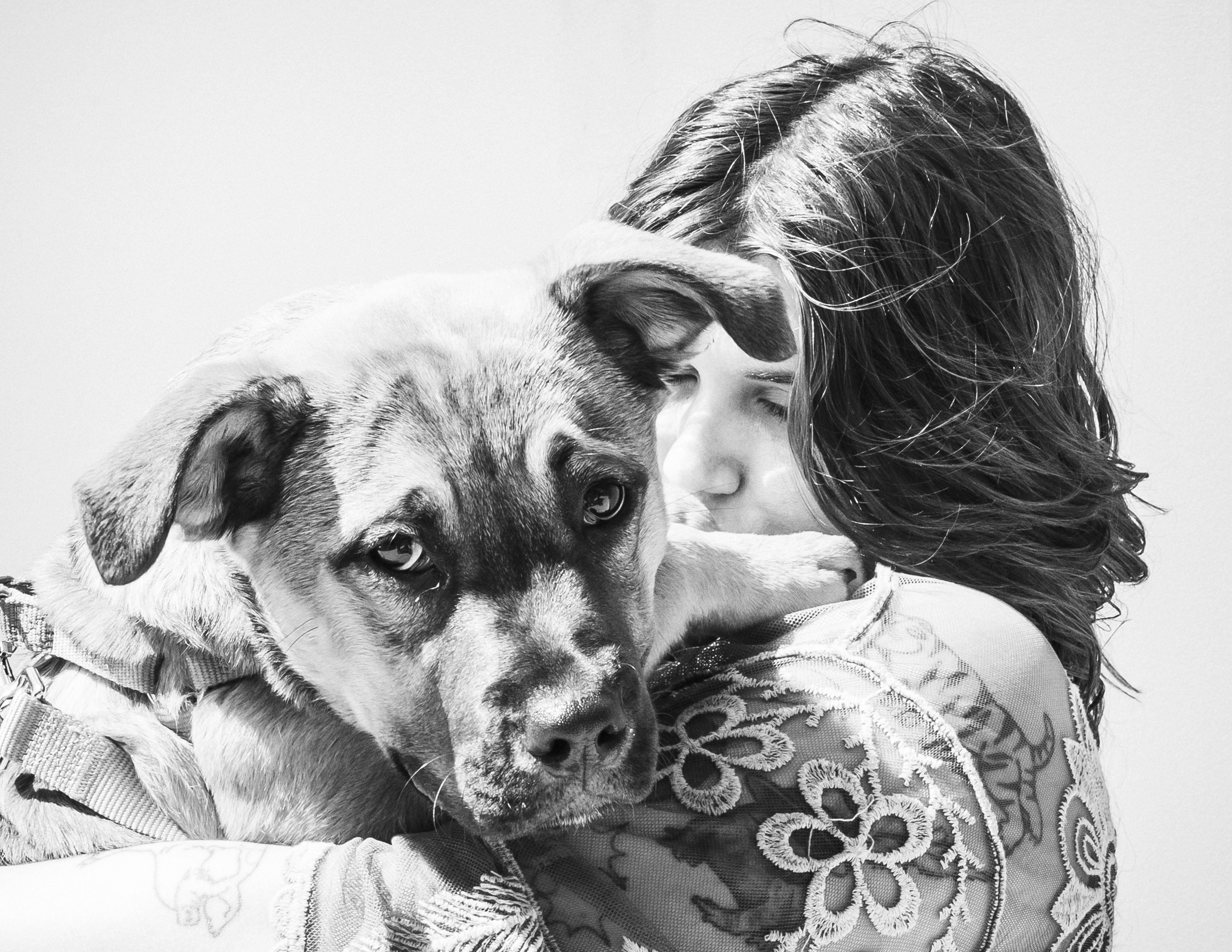A young woman snuggles into her puppy, in black and white.